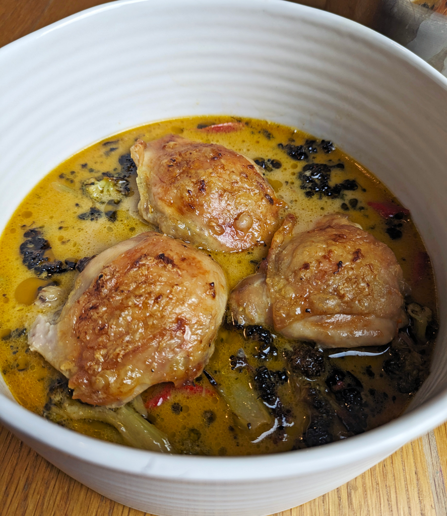 Crispy-skinned chicken thighs in a yellow sauce of coconut milk and spices with flecks of deep green from the charred roasted broccoli