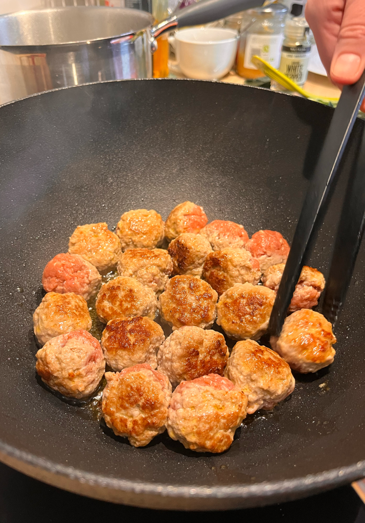 Five Spice Meatballs Frying in hot wok and being turned with tongs.