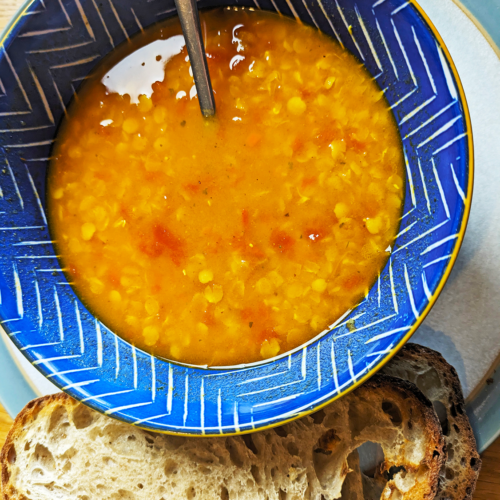 A bowl of spicy tomato lentil soup with sourdough bread