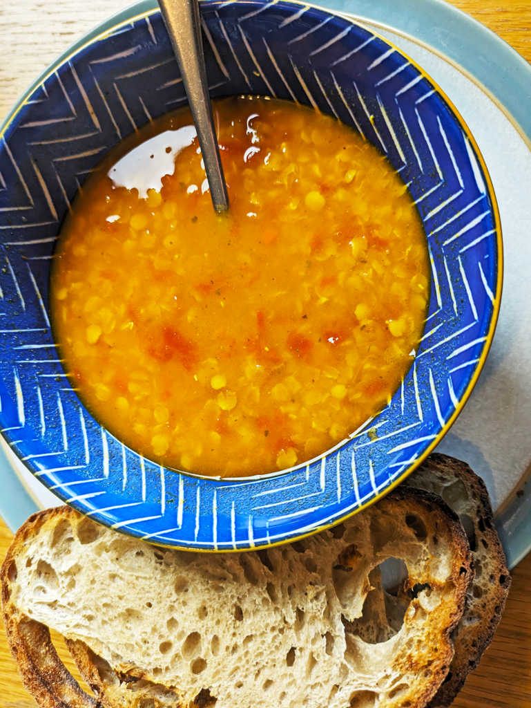 A bowl of spicy tomato lentil soup with sourdough bread